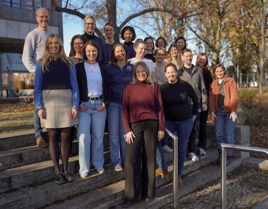 Gruppenfoto mehrerer Personen im Freien vor Bäumen und einem Gebäude.
